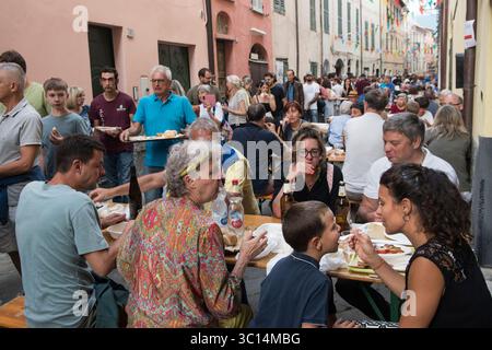 Madre e figlio italiani, lei lo nutre dal suo cucchiaio. Una madre punteggiata, credo che non sia sicuro se gli piacerà ciò che è stato convinto a provare all'annuale festival di barbabietole Borgomaro nel villaggio medievale di montagna. La strada principale è fiancheggiata da tavoli, la folla è in fila per raccogliere piatti di cozze. Borgomaro, regione Liguria, Italia, Europa. Luglio 2025 HOMER SYKES Foto Stock