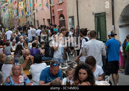 Festival gastronomici in Italia. La festa annuale delle cozze di Borgomaro nel borgo medievale di montagna. La strada principale è fiancheggiata da tavoli, folle di persone mangiano piatti di molluschi e cozze. Borgomaro, regione Liguria, Italia, Europa. Luglio 2025 HOMER SYKES Foto Stock