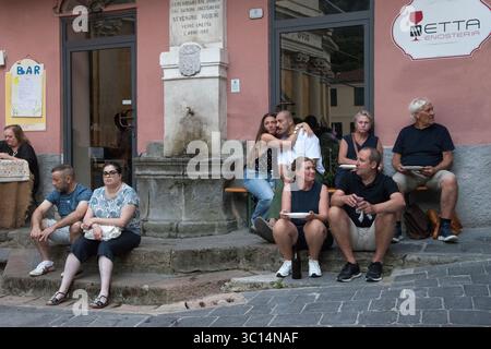 Borgomaro Italia. I turisti e gli abitanti del luogo che partecipano all'annuale festival di conchiglie si trovano in Piazza felice Cascione e guardano il mondo che passa. Borgomaro, regione Liguria, Italia, Europa. Luglio 2025 HOMER SYKES Foto Stock
