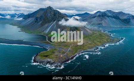 Le viste mozzafiato della costa delle Icelands rivelano torreggianti montagne avvolte da nebbia, lussureggianti campi verdi e vivaci acque blu. Questo splendido paesaggio mostra la natura della riserva naturale delle Hvalnes Foto Stock