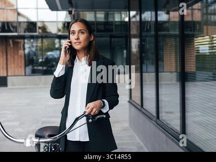 Giovane donna elegante in abiti formali neri con bicicletta Foto Stock
