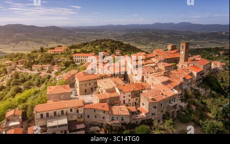 Veduta aerea dei tetti di terracotta che scendono lungo la collina, coronati dalla torre dell'orologio nell'antico villaggio di Vetulonia, Italia. Foto Stock