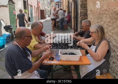 Festival gastronomici in Italia. L'annuale festa dei molluschi di cozze Borgomaro nel borgo medievale italiano di montagna. La gente della strada principale, che apre i molluschi, prepara il pasto per la prossima sera. Borgomaro, regione Liguria, Italia, Europa. Luglio 2025 HOMER SYKES Foto Stock