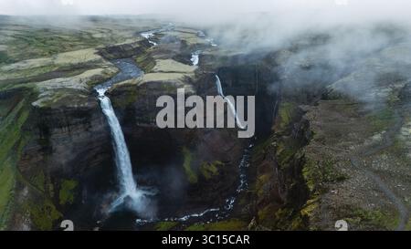 La cascata di Haifoss scorre potente sopra ripide scogliere, creando splendide cascate nel mezzo del terreno accidentato delle ghiacciaie. La nebbia sorge, esaltando il mistero di questa meraviglia naturale durante un pomeriggio nuvoloso. Foto Stock
