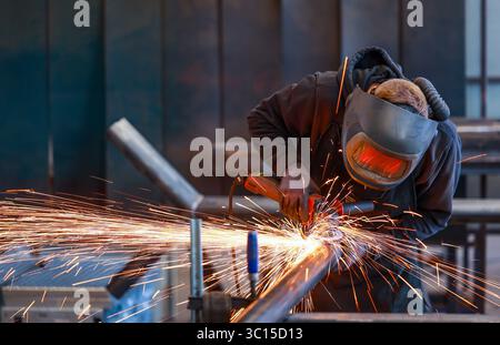Germania - foto a tema: Industria metallurgica. Un lavoratore industriale taglia un tubo in acciaio con una smerigliatrice angolare. Foto Stock
