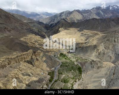 Vista aerea di una valle scolpita da un fiume con campi verdi e lontane montagne innevate sotto un cielo nuvoloso, Leh, Ladakh, India. Foto Stock