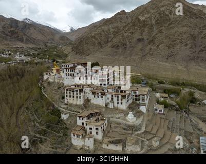 Vista aerea degli edifici bianchi del monastero che contrastano con il terreno aspro e montuoso, punteggiato da una statua dorata, Leh, Lad Foto Stock