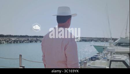 Uomo in piedi che indossa un cappello di paglia, una camicia rosa che afferra il palo della cordicella al molo del porticciolo, con yacht Foto Stock