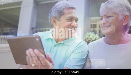 Coppia sorridente seduto sul portico anteriore, tenendo un tablet vicino a colonne bianche e piante in vaso Foto Stock
