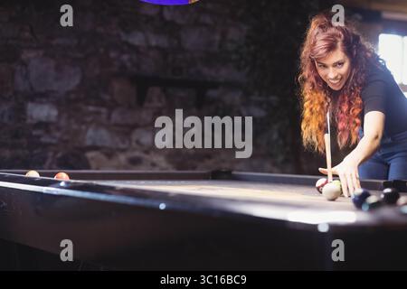 Donna che ha sparato sul tavolo da biliardo nella sala giochi con il bastoncino di puntino sulle palle, spazio copia Foto Stock