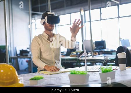 Il visore per la realtà virtuale si trova tra i modelli di turbina eolica di un computer portatile sulla scrivania in un ufficio moderno Foto Stock