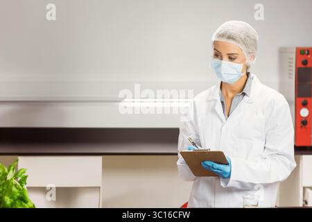 Portadocumenti e penna appoggiati accanto al bicchiere in vetro con liquido trasparente su banco in acciaio vicino all'incubatore Foto Stock