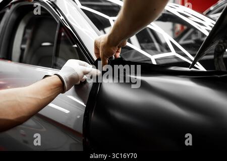 Rivestimento in vinile per auto a pannello intero. L'installazione di un involucro in vinile su larga scala trasforma l'esterno del veicolo con una pellicola nera opaca. Modifiche all'applicazione di avvolgimento per auto Foto Stock