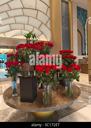 Elegante disposizione di rose rosse in vasi di vetro su un tavolo in marmo, creando un ambiente lussuoso con elementi decorativi Foto Stock