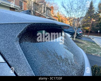 Un'auto con un finestrino posteriore smerigliato si trova in un vialetto. L'auto è parcheggiata accanto a una casa con un camino Foto Stock