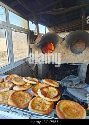 Il pane appena sfornato poggia su un tavolo vicino a un forno tradizionale, mostrando colori caldi e un'atmosfera rustica da cucina Foto Stock
