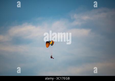 Una persona sta sorvolando le nuvole con un vibrante parapendio in un cielo azzurro. L'attività mette in mostra l'emozione del parapendio, sullo sfondo di morbide e soffici nuvole. Foto Stock