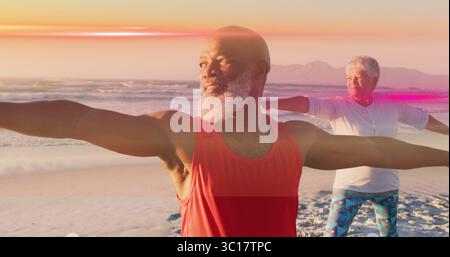 Una coppia che indossa un abbigliamento sportivo e tiene in posa il Guerriero II sulla spiaggia sabbiosa al tramonto e alle onde dell'oceano Foto Stock