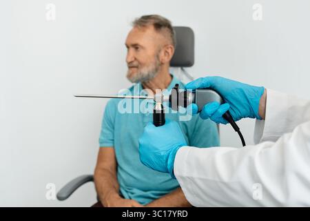 Medico con endoscopio per endoscopio video endoscopico nelle mani per controllare gli organi otorinolaringoiatrici durante la procedura di esame di un anziano seduto su una sedia ORL Foto Stock