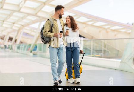 Uomo e donna che attraversano l'aeroporto con bagagli e caffè da asporto Foto Stock