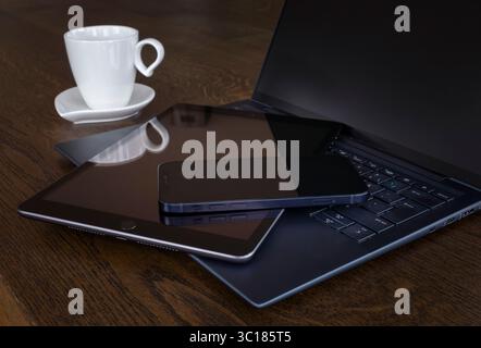 Moderno spazio di lavoro con computer portatile, tablet, smartphone e tazza da caffè su una scrivania in legno per lavorare in remoto. Immagine perfetta per il lavoro e il freelance Foto Stock