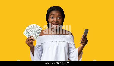 Concetto di cashback. Smartphone di Young Woman Holding e Dollar Cash eccitati Foto Stock