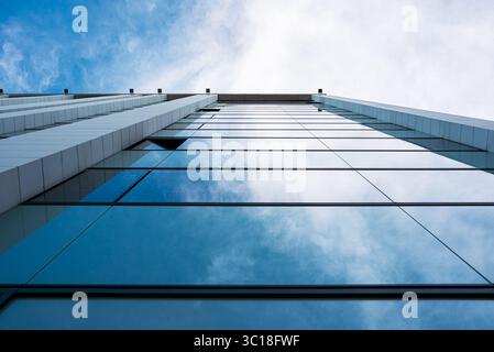 Prospettiva verticale di un edificio moderno con finestre riflettenti contro un cielo blu chiaro Foto Stock