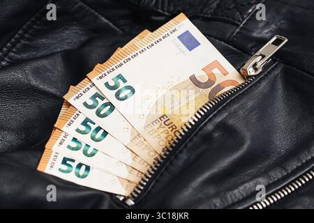 Cinquanta euro in tasca. Denaro nascosto all'interno di una giacca di pelle. Primo piano della tasca con cerniera. Risparmi finanziari o attività illecite. Banconote in euro. Foto Stock