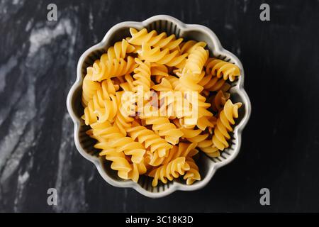 Penne crude nel recipiente. Spaghetti secchi gialli su sfondo scuro. Primo piano sui maccheroni italiani crudi. Ingredienti alimentari tradizionali. Pasto semplice e salutare. Foto Stock