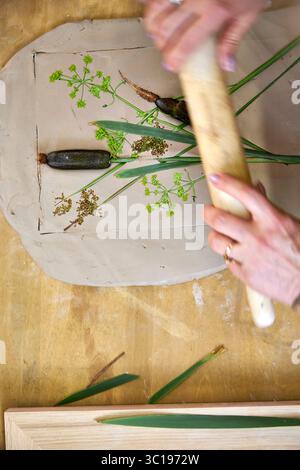 Premendo fiori e foglie in argilla con un mattarello per creare un'impronta botanica per il rilievo gesso. Mani appiattimento piante in fai da te passo per passo t Foto Stock