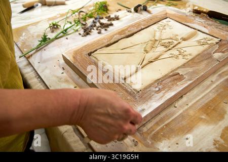 Mani che tengono il rilievo in gesso botanico finito in una cornice di legno. Opere d'arte floreale fai da te con stampe di fiori e foglie, fase finale del decoro fatto a mano Foto Stock