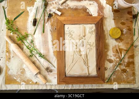 Rilievo in gesso botanico finito in una cornice in legno con impronte floreali. Risultato artistico fatto a mano fai da te, decorazioni floreali creative realizzate passo dopo passo Foto Stock