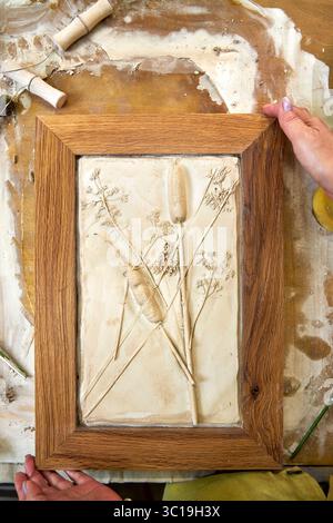 Rilievo in gesso botanico finito in una cornice in legno con impronte floreali. Risultato artistico fatto a mano fai da te, decorazioni floreali creative realizzate passo dopo passo Foto Stock