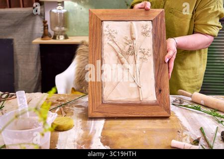 Persona che detiene un rilievo in gesso botanico completato in telaio di legno. Opere d'arte floreali fatte a mano con stampe floreali, risultato finale del fai da te passo dopo passo Foto Stock