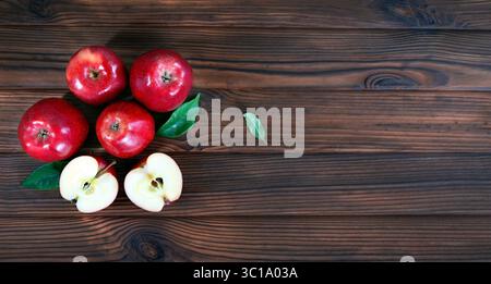Mele rosse fresche su una superficie rustica in legno. Una vista dall'alto di cinque mele rosse fresche poste su una superficie rustica in legno, due delle quali sono tagliate a fette per rivelarsi Foto Stock