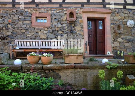 Facciata in pietra con porta in legno, panca e decorazione floreale Foto Stock