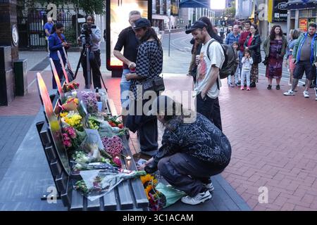 Broad Street, Birmingham, 22 luglio 2025: I fan di Ozzy Osbourne sono venuti al Black Sabbath Bridge di Birmingham in Broad Street per rendere omaggio a Ozzy Osbourne, morto all'età di 76 anni. Fiori, biglietti e candele sono stati lasciati sulla panchina e alcune persone hanno bevuto qualcosa e li hanno condivisi con l'immagine di Ozzy sulla panchina. Crediti: British News and Media/Alamy Live News Foto Stock
