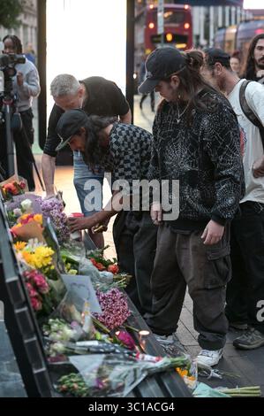 Broad Street, Birmingham, 22 luglio 2025: I fan di Ozzy Osbourne sono venuti al Black Sabbath Bridge di Birmingham in Broad Street per rendere omaggio a Ozzy Osbourne, morto all'età di 76 anni. Fiori, biglietti e candele sono stati lasciati sulla panchina e alcune persone hanno bevuto qualcosa e li hanno condivisi con l'immagine di Ozzy sulla panchina. Crediti: British News and Media/Alamy Live News Foto Stock