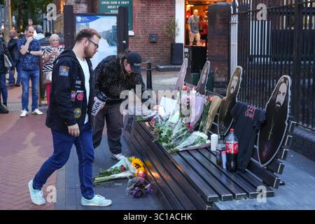 Broad Street, Birmingham, 22 luglio 2025: I fan di Ozzy Osbourne sono venuti al Black Sabbath Bridge di Birmingham in Broad Street per rendere omaggio a Ozzy Osbourne, morto all'età di 76 anni. Fiori, biglietti e candele sono stati lasciati sulla panchina e alcune persone hanno bevuto qualcosa e li hanno condivisi con l'immagine di Ozzy sulla panchina. Crediti: British News and Media/Alamy Live News Foto Stock