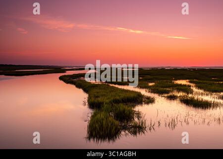 Il bagliore arancione dell'alba si riflette sulla palude salata di Hamlin Creek nell'estuario di Cape Romain a Isle of Palms, South Carolina. Foto Stock