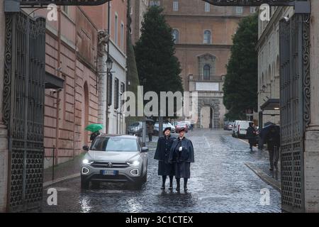 VATICANO - 15 GENNAIO 2025: Due guardie svizzere, in caso di pioggia buia, sono in guardia su ciottoli bagnati all'interno di una porta in ferro battuto che conduce al Vaticano. Foto Stock