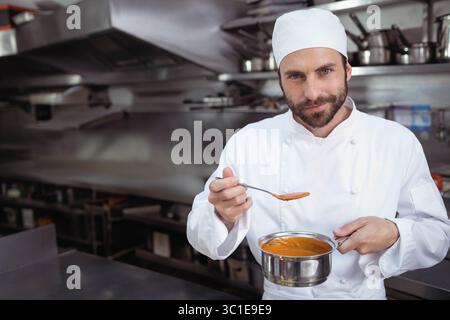 Chef maschile professionista che tiene in mano una pentola e degusta zuppa di pomodoro in cucina commerciale, spazio per copiare Foto Stock