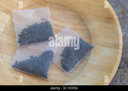 Tre bustine di tè in rete riempite di tè nero sfuso sono poste su un piatto rotondo di legno. Foto Stock