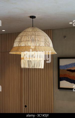 Grande lampada a sospensione in rattan o bambù intrecciata appesa in una camera moderna. Design degli interni in stile bohémien o giapponese. Arredi naturali e sostenibili. Foto Stock