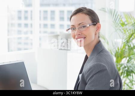 Donna d'affari seduta alla scrivania in ufficio con un blazer grigio che utilizza laptop e spazio per copiare Foto Stock