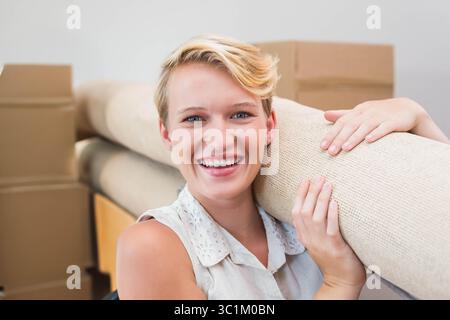 Donna che indossa una blusa senza maniche che tiene un tappeto beige arrotolato sulla spalla in camera con le scatole mobili Foto Stock