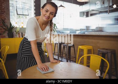 Cameriera donna che indossa un grembiule a righe appoggiato su un panno di legno sotto le lampade a sospensione Foto Stock