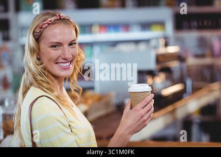 Donna che sorride e tiene in mano una tazza di caffè di carta costolata al bancone del caffè con macchina per espresso e spazio per fotocopie Foto Stock
