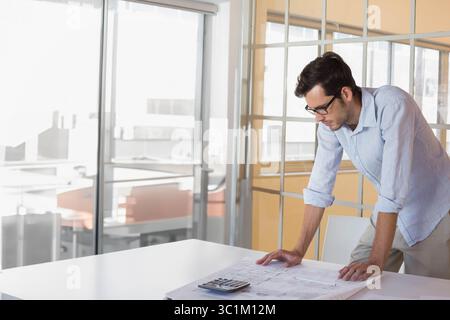 Uomo adulto professionista che si appoggia al tavolo studiando i progetti e utilizzando la calcolatrice nella sala riunioni Foto Stock