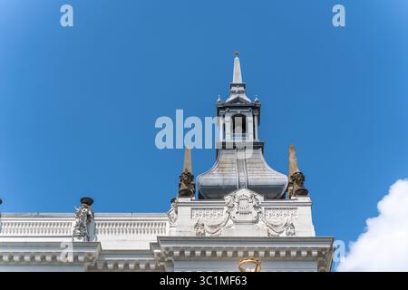 Un tetto storico con un tetto riccamente decorato e una torre centrale contro un cielo blu. L'architettura presenta ornamenti e figure classiche. Foto Stock